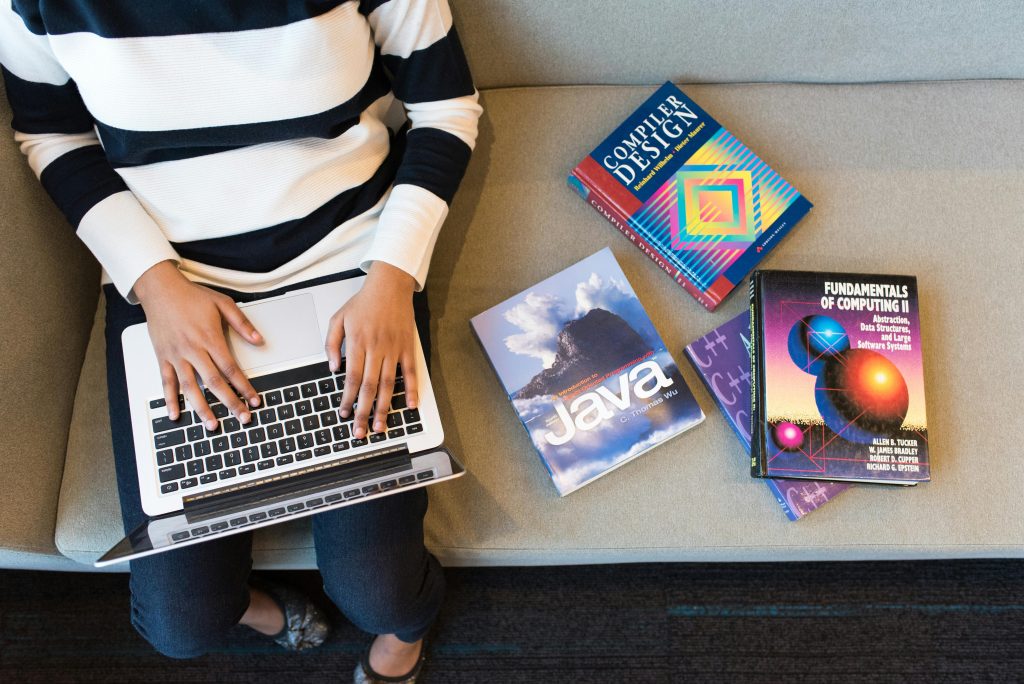 pexels-photo-1181298-1181298 Woman using laptop on sofa, surrounded by programming books, learning coding.
