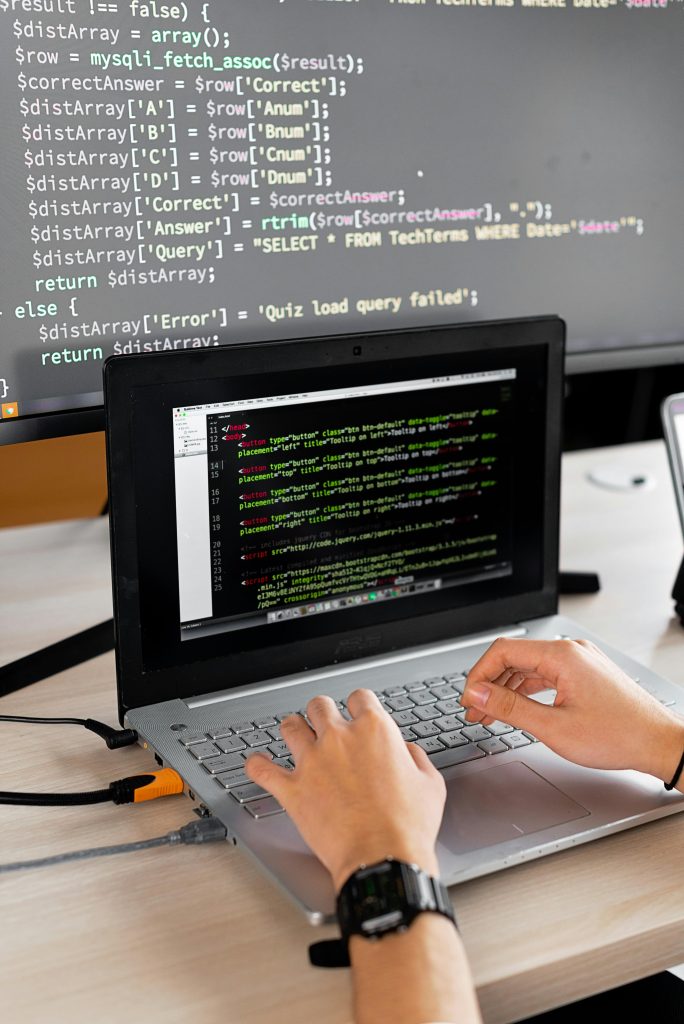 pexels-photo-7988086-7988086 Person coding at a desk with laptop and external monitor showing programming code.